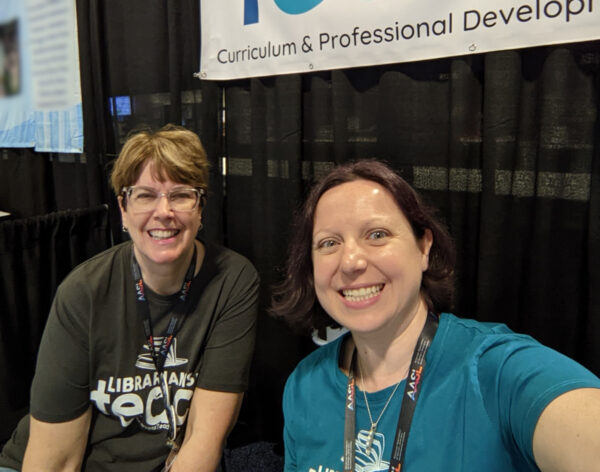 Cari and Collette, co-founders, wearing charcoal gray and teal logo t-shirts.